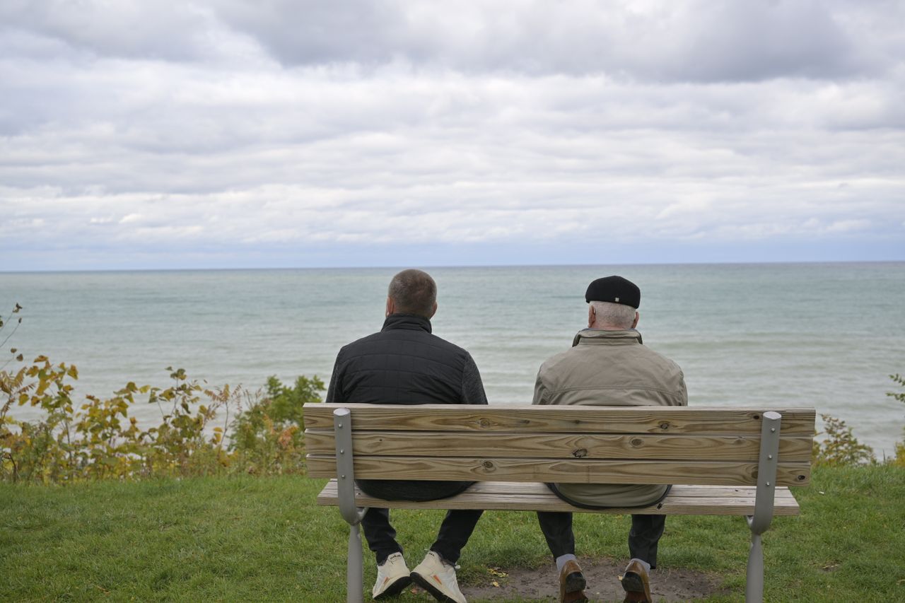 Two men sitting on a bench by the ocean, sharing a peaceful moment by the sea.